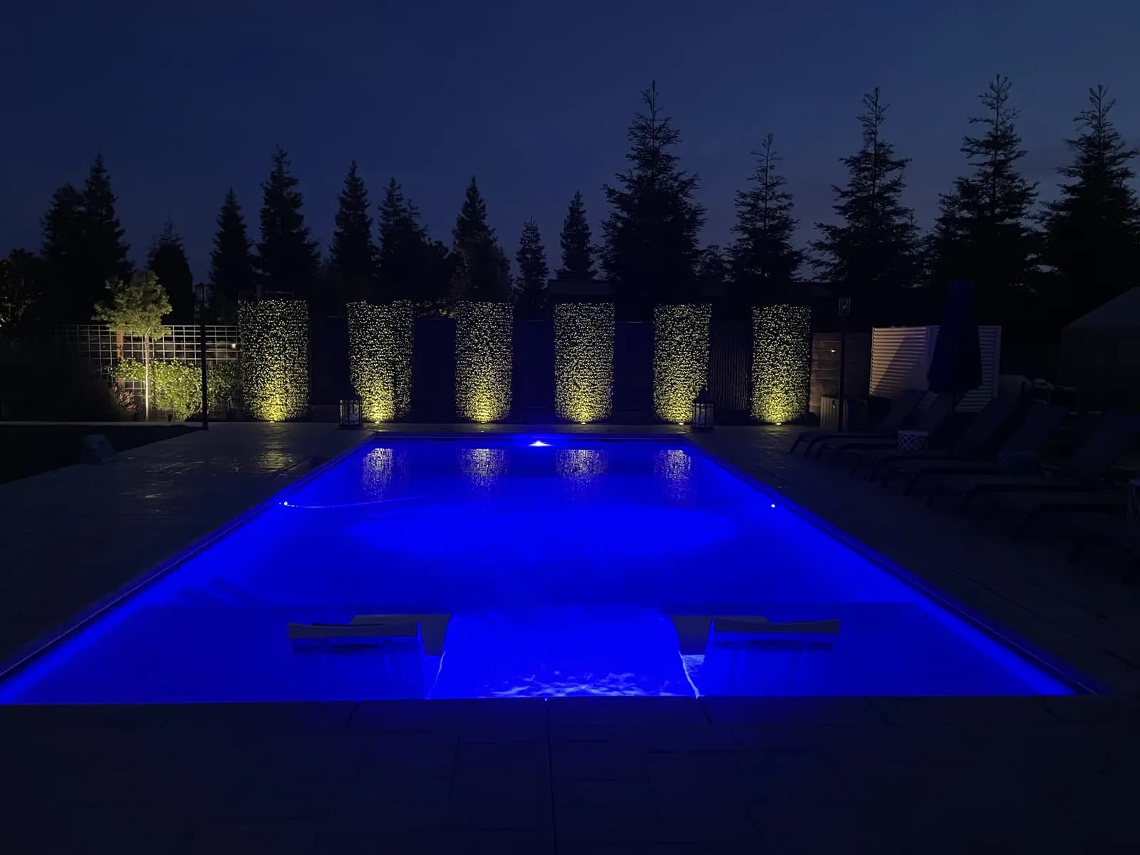 Pool glowing blue with uplit hedges behind it