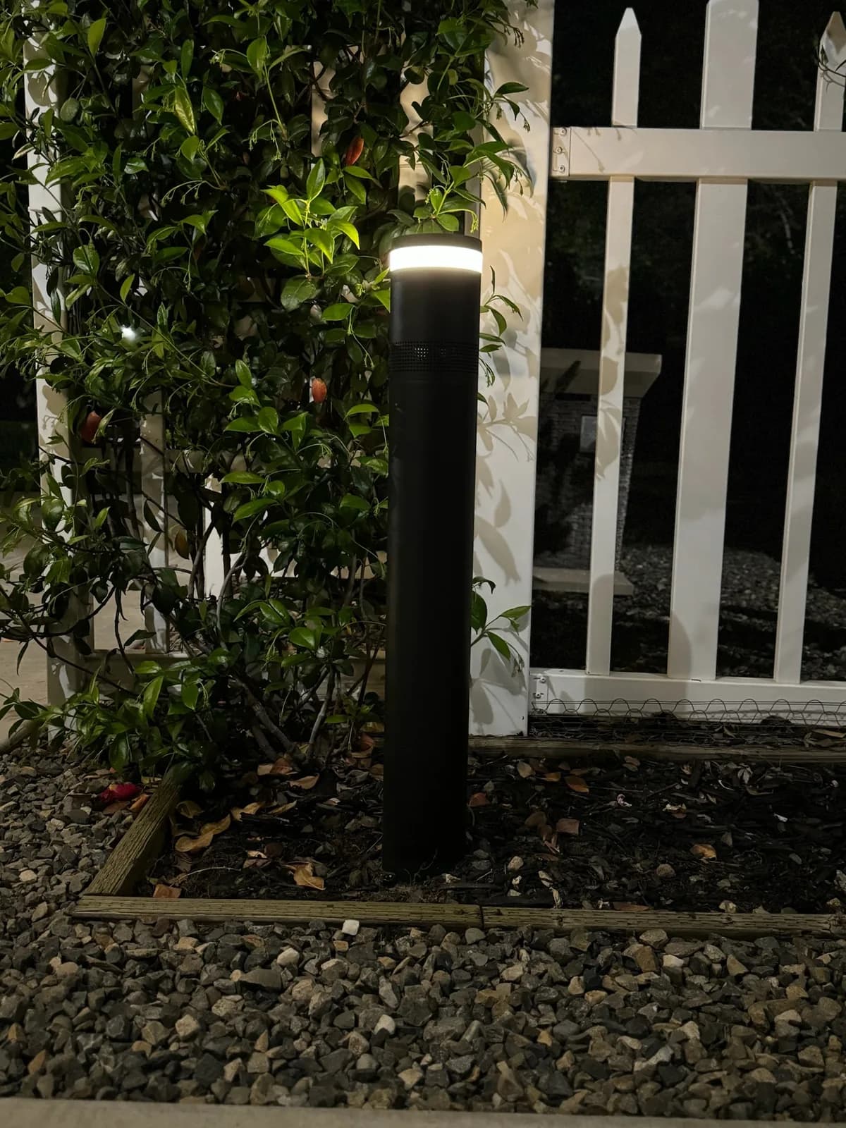 Modern bollard beside a white picket fence
