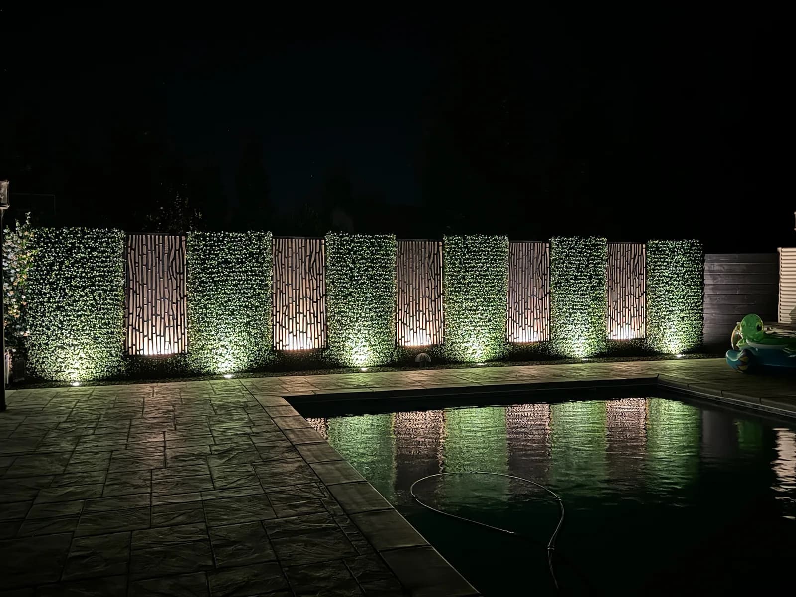 Uplit hedge panels reflected in a pool